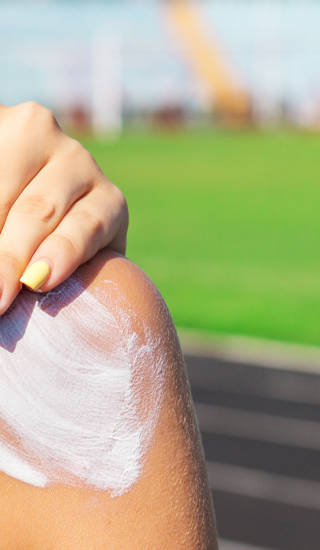 Fitness woman is applying sunscreen on her shoulder before training at the stadium. Protect your skin during sport activity.